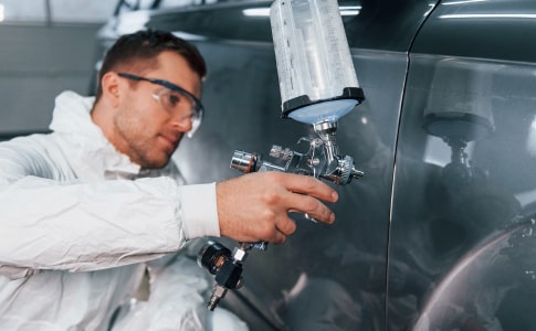 Technician applying Sherwin-Williams paint finish to a car in a spray booth
